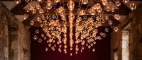 Stunning copper spherical pendant lights create dramatic ceiling installation in rustic stone interior space for luxury hospitality design.