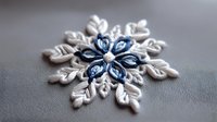 White and blue decorative snowflake ornament with delicate floral pattern and crystal details captured in macro photography on gray textured background.