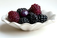Fresh ripe blackberries, raspberries and dark grape in white ceramic bowl with wavy edges on light background, macro food photography.