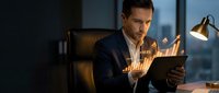 Professional businessman analyzing financial data on tablet with holographic charts in modern office during evening hours for business strategy planning.