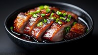 Sliced glazed duck breast with green onions in black ceramic bowl, served with sweet soy sauce. Dark moody food photography on black background.
