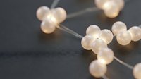 Warm glowing spheres on delicate wire strands create soft bokeh lighting effects against dark background, suitable for festive decorations and ambient lighting design projects.