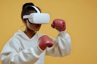 Young African American woman in white hoodie wearing VR headset and red boxing gloves against yellow background, ready for virtual fitness training session.