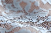 Delicate white lace fabric with intricate floral pattern creates soft texture and depth against pink background, macro photography reveals detailed mesh structure.