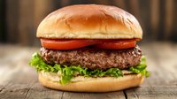 Fresh beef burger with lettuce, tomato and soft bun on rustic wooden background. Classic American fast food sandwich photographed with selective focus.