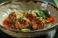 Asian style meatballs in spicy sauce garnished with green onions and bok choy served in ceramic bowl, close up view of traditional Asian cuisine.