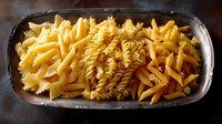 Various uncooked pasta types including fusilli, penne and rotini arranged in rows on dark plate, showcasing traditional Italian dry pasta varieties for cooking.