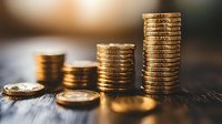 Stacked gold coins showing increasing financial growth on wooden surface with warm lighting and shallow depth of field.