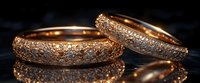 Luxurious rose gold wedding bands with pavé diamonds on black reflective surface, elegant jewelry photography showing intricate details and sparkle.