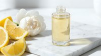 Lemon essential oil in glass bottle with fresh citrus slices and white peony flower on marble surface for aromatherapy and skincare.