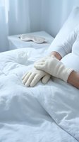 Patient hands in white medical gloves resting on hospital bed with clean white linens in sterile healthcare environment for medical treatment and recovery.