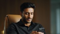 Young professional businessman using smartphone in modern office chair, focused on mobile device screen for business communication and digital connectivity.