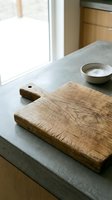Rustic wooden cutting board with weathered texture on modern kitchen counter with ceramic bowl and natural lighting for culinary preparation.