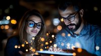 Young diverse couple looking at glowing digital tablet in dark room with magical bokeh light effect, technology concept for digital innovation.