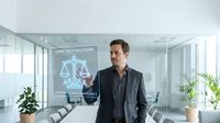 Professional businessman in dark suit standing in modern glass office conference room with legal tech solutions holographic display and scales of justice symbol.