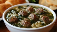 Italian wedding soup with tender meatballs, orzo pasta, fresh spinach and herbs in clear broth served in white ceramic bowl, traditional comfort food.