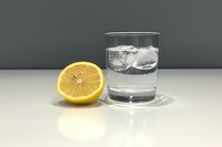 Glass of pure water with ice cubes and fresh cut lemon half on white surface against gray background, minimalist drink composition for healthy lifestyle.