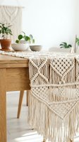 Boho macrame table runner with intricate knotted patterns on wooden dining table. Handcrafted textile decoration with fringe details for modern home interior styling.