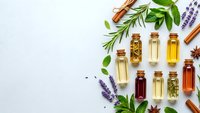Essential oils in glass bottles with fresh herbs, lavender, rosemary, mint and cinnamon sticks on white background for aromatherapy and natural wellness.
