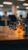 Orange pawn standing out among gray chess pieces on wooden board in blurred office setting, symbolizing leadership, strategy, and competitive advantage for business concepts.