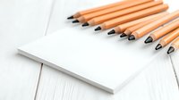 Orange wooden pencils arranged on white paper notebook for drawing sketching and creative writing projects on rustic wooden surface background.