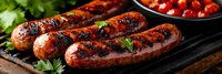 Grilled bratwurst sausages with char marks on barbecue grill, garnished with fresh herbs and cherry tomatoes for outdoor cooking and summer dining.