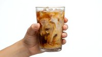 Hand holding glass of cola with ice cubes on white background, isolated beverage for advertising, restaurant menus, and drink promotion designs.