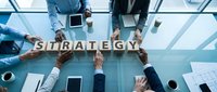 Business team collaborating around conference table with wooden letter blocks spelling STRATEGY in modern office meeting room for corporate planning.