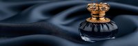 Elegant dark blue glass perfume bottle with ornate golden cap on luxurious silk fabric background with soft folds creating dramatic lighting effect.