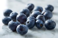 Fresh ripe blueberries with water drops scattered on marble surface in soft natural light, macro food photography for healthy eating and recipe blogs.