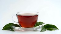 Hot tea in transparent glass cup with saucer and fresh green leaves on white background. Warm beverage for relaxation and wellness lifestyle.
