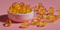Golden vitamin E capsules spilling from white bowl on pink background. Health supplement omega oil pills for wellness and nutrition care.