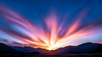 Dramatic sunset over mountain landscape with vibrant orange, pink, and purple sky rays bursting from horizon, suitable for backgrounds and nature themes.