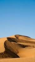 Golden sand dunes with dramatic shadows and ripple patterns against clear blue sky. Suitable for travel, nature, and desert landscape backgrounds.