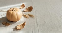Autumn harvest composition with orange pumpkin, dried oak leaves and wheat stalks on neutral linen background for seasonal decoration and thanksgiving themes.