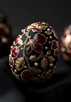 Luxurious black Easter egg decorated with gold filigree, red gemstones and pearls featuring intricate floral pattern on dark background. Elegant holiday ornament.