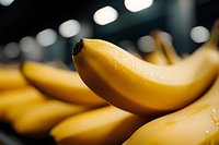 Fresh ripe yellow bananas with water drops in macro view against dark blurred background with bokeh lights, selective focus on single banana.