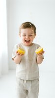 Young toddler, Caucasian, wearing beige linen clothing, joyfully squeezing fresh lemons with juice splashing. Perfect for food, healthy eating, children's nutrition, and lifestyle content.