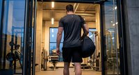 Athletic man entering modern gym facility carrying sports bag ready for workout session.