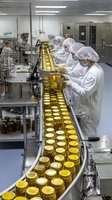 Workers in protective clothing inspecting honey jars on automated production line in modern food processing facility.
