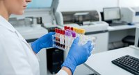 Laboratory technician in blue gloves holding test tubes with colorful samples in modern medical research facility for scientific analysis and testing.