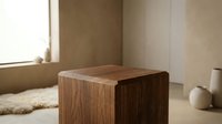 Minimalist wooden cube side table with rich walnut grain texture in a warm, neutral Scandinavian interior with soft natural light.