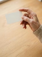 Mature adult male hand holding blank white business card on wooden surface for branding and corporate identity mockup use.