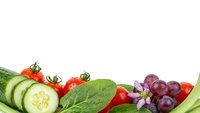 Fresh organic vegetables and fruits border with cucumber slices, cherry tomatoes, spinach leaves and red grapes on white background for healthy eating.