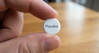 Hand holding white placebo pill tablet for medical research study and clinical trial testing pharmaceutical drug development.