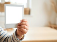 Toddler's hand holding blank white instant photo frame with striped sleeve in bright home interior, suitable for mockups and creative projects.