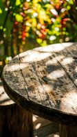 Weathered wooden table surface with sharp focus in foreground, blurred vibrant garden foliage with yellow and red flowers in background, natural sunlight creating dappled shadows, outdoor setting.