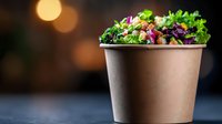 Fresh mixed salad with grilled chicken, vegetables and greens in eco-friendly paper bowl on dark background with bokeh lights. Food delivery concept.
