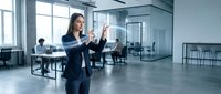 Young Caucasian businesswoman interacting with glowing holographic interface in modern office, colleagues working in background, futuristic technology concept.