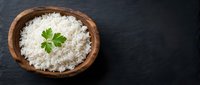 Cooked white rice in wooden bowl with fresh parsley garnish on dark slate background, healthy grain side dish for Asian and international cuisine.